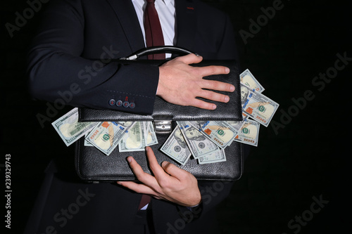 Businessman holding briefcase with dollar banknotes on dark background. Corruption concept photo