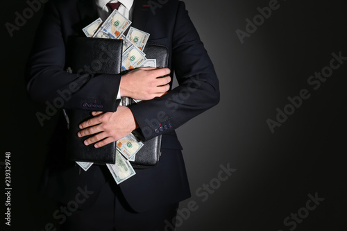 Businessman holding briefcase with dollar banknotes on dark background. Corruption concept