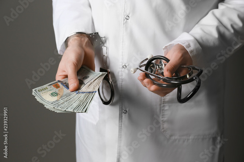 Doctor in handcuffs and with bribe on grey background. Corruption concept