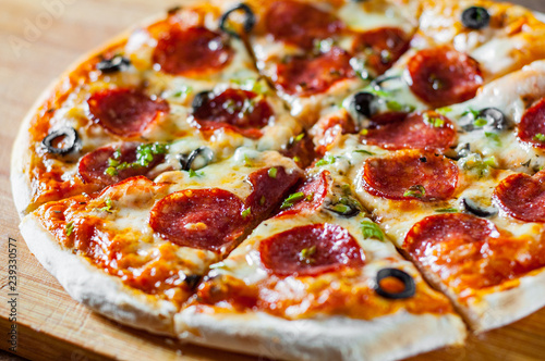 Pizza with Mozzarella cheese, pepperoni, tomato, pepper, olive, salami. Italian pizza on wooden table background