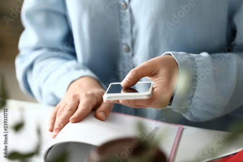 Woman with mobile phone reading book at table. Concept of study