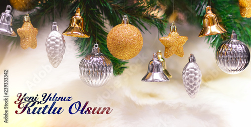 Shiny gold and silver christmas balls, stars and bells on white with pine tree. Yeni yılınız kutlu olsun means happy new year photo