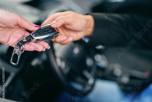 Close up of woman giving car keys to man in car. Selective focus on hands.