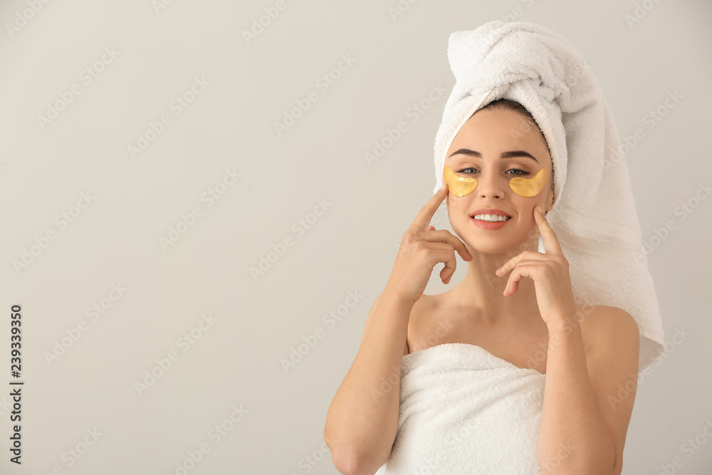 Beautiful young woman with under-eye patches on light background