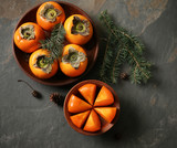 Plates with whole and cut ripe persimmons on grey table