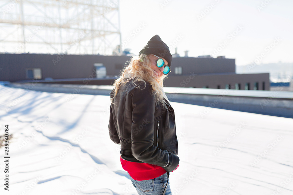 outdoor winter portrait pretty charming blonde woman wearing black cap and jacket on the roof in sunlight