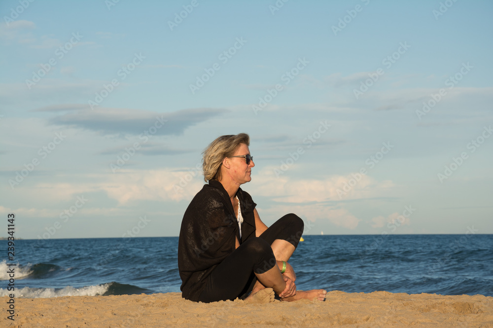Frau am Strand mit Sonnenbrille sitzend