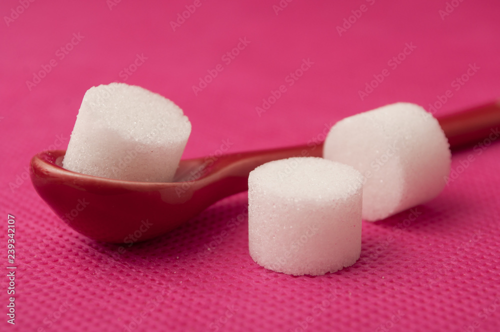 closeup of sugar in shaped circle in red spoon on pink background closeup of sugar in shaped circle in red spoon on pink background