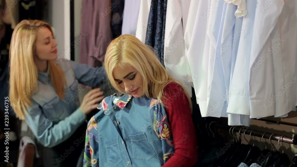 Two fashionable blonde girls choose clothes in a large clothing store. Slender young women buy fashionable clothes in a modern shopping center. Two fashionable blonde girls choose clothes in a large clothing store. Slender young women buy fashionable clothes in a modern shopping center.