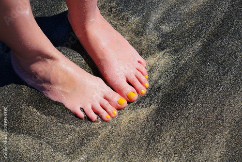 Pair of bare feet with yellow nail polish and a toe crystal at the beach