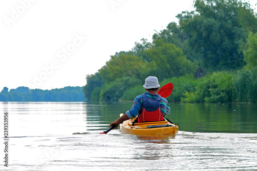 Rear view of kayaker man paddle yellow kayak on Danube river. Summer kayaking. Concept for adventure, travel, action, lifestyle