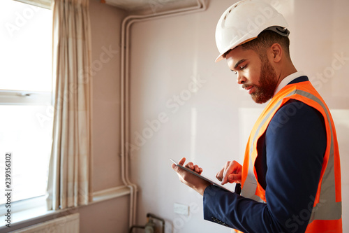 Surveyor In Hard Hat And High Visibility Jacket With Digital Tablet Carrying Out House Inspection photo