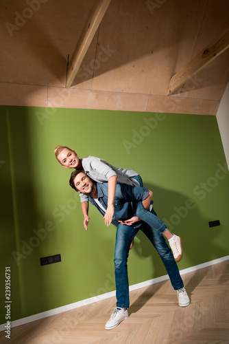 handsome man giving piggyback ride to attractive girl in apartment