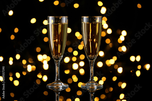 Glasses of tasty champagne on dark background against defocused lights