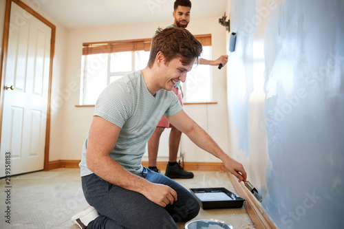 Fotografie Two Men Decorating Room In New Home Painting Wall Together