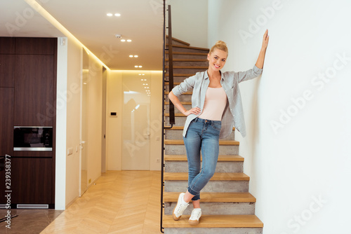 beautiful girl standing on stairs, smiling and looking at camera at home