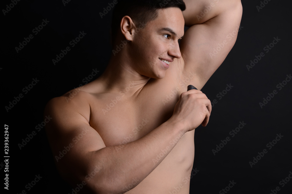 Young man using deodorant on dark background Young man using deodorant on dark background