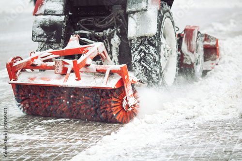 City service cleaning snow , a small tractor with a rotating brush clears a road in the city park from the fresh fallen snow on winter day, brush - close-up.