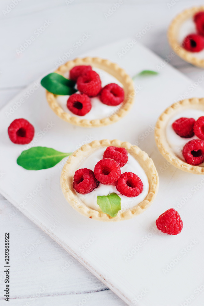 Tartlets with cream and raspberry on a white wooden board Tartlets with cream and raspberry on a white wooden board