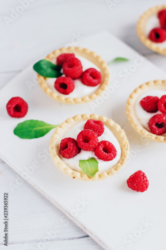 Tartlets with cream and raspberry on a white wooden board