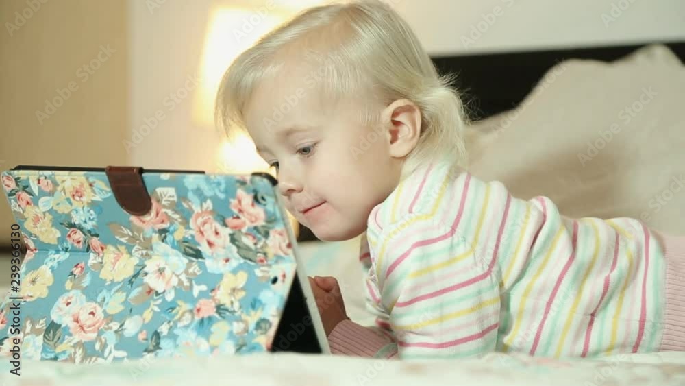 Smiling blonde little girl on a bed with a tablet computer Smiling blonde little girl on a bed with a tablet computer