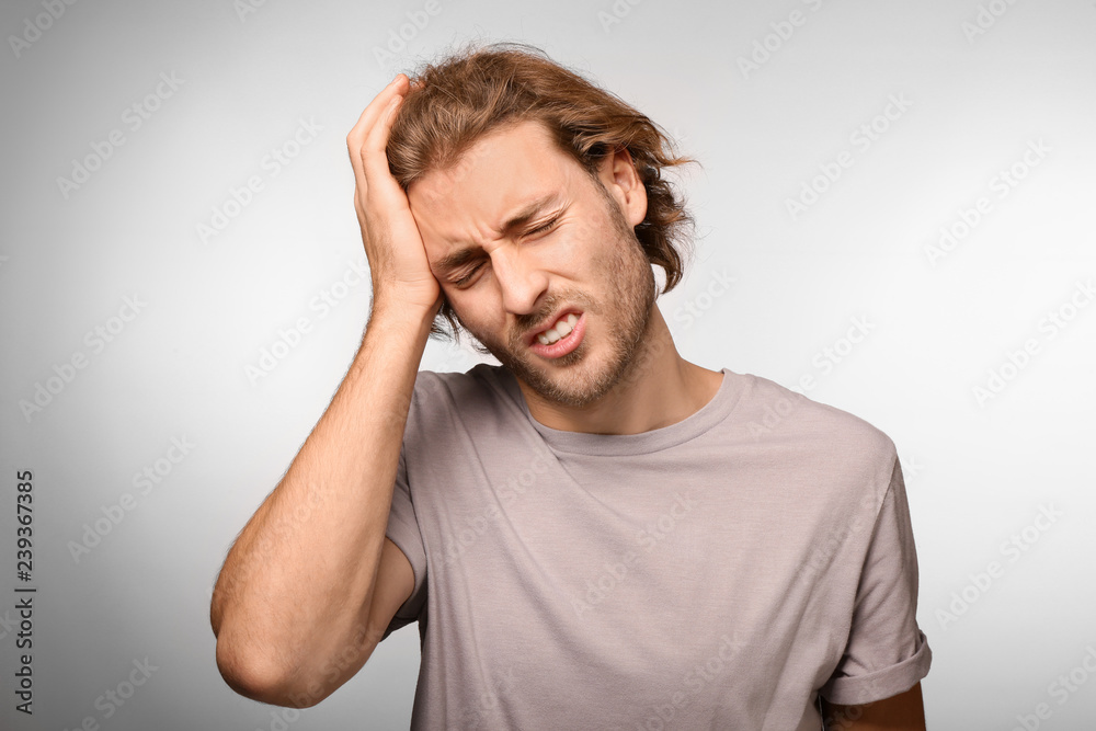 Young man suffering from headache on light background Young man suffering from headache on light background