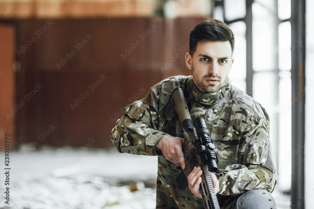 A young military soldier sits with a big rifle in his hands, near the window of a collapsed building! Secret Operation of US Soldiers A young military soldier sits with a big rifle in his hands, near the window of a collapsed building! Secret Operation of US Soldiers