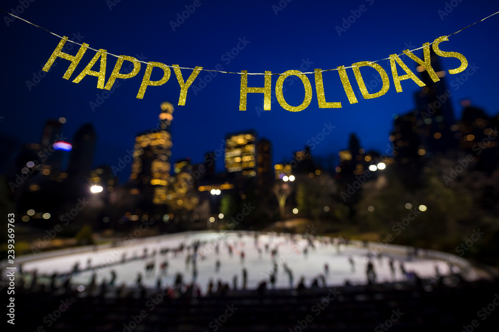 Happy Holidays message in shiny gold letters hanging in the winter sky above a busy ice skating rink surrounded by twinkling city lights