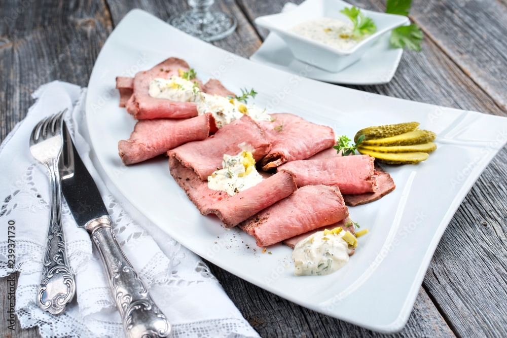 Traditional lunch meat with sliced cold cuts roast beef and remoulade as closeup on a white plate on a wooden table Traditional lunch meat with sliced cold cuts roast beef and remoulade as closeup on a white plate on a wooden table