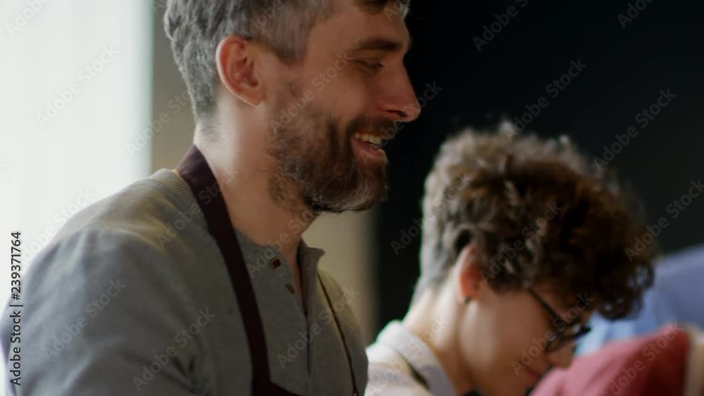 Caucasian man on foreground smiling and holding vegetable shashlik in hands while others on background cooking Caucasian man on foreground smiling and holding vegetable shashlik in hands while others on background cooking