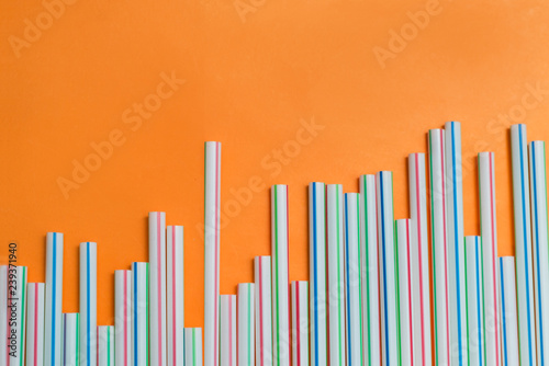 Striped drink straws of different colors in row isolated on orange background. Minimalism concept. Pop art style. Flat lay with straws used for drinking water or soft drinks. Copy