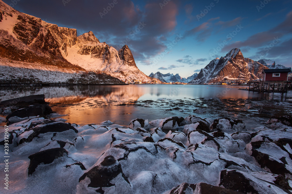 View of beautiful Reine village in winter time with montains in background with light of sunrise. Lofoten, Norway.