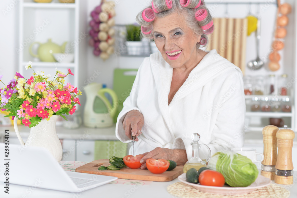 Senior woman in hair rollers cutting vegetables on kitchen Senior woman in hair rollers cutting vegetables on kitchen
