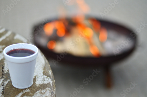 Tisch mit Becher voller Glühwein im Hintergrund ein Feuer