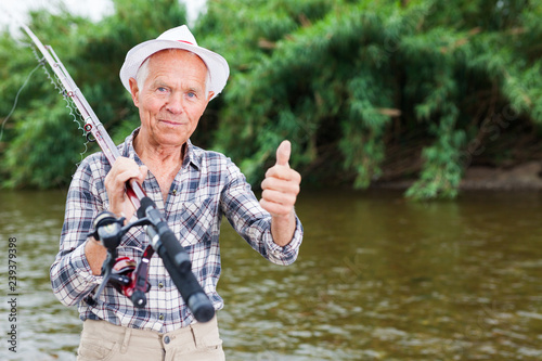 Mature fisherman with rod at riverside