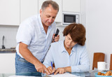 Mature couple  at table in home kitchen, woman filling up documents