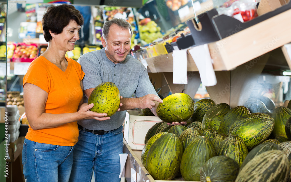 Fototapeta premium Glad man and his wife are choosing ripe melon