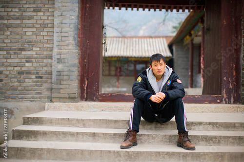 Young man sitting on some steps in front of a traditional Chinese building.