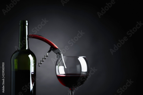 Red wine with corkscrew on a black background.