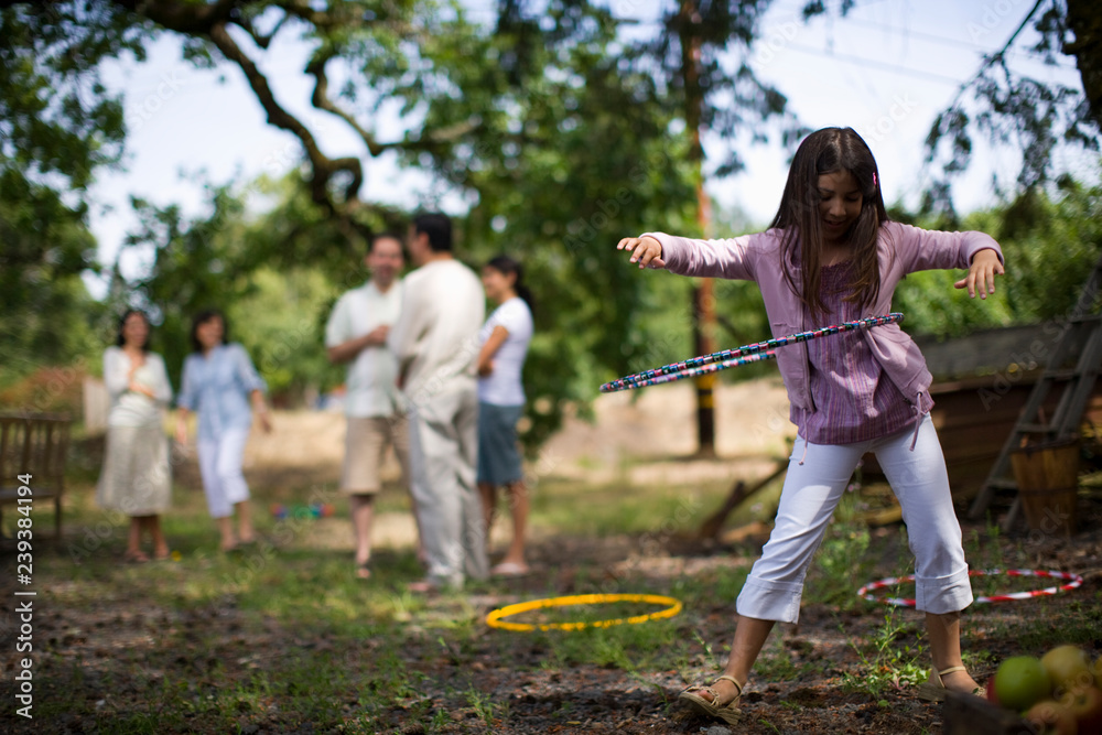 A young girl hula-hooping while her family stand in the background A young girl hula-hooping while her family stand in the background
