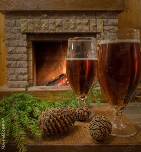 Two beer glasses, cones, christmas tree branch against cozy firepace. photo