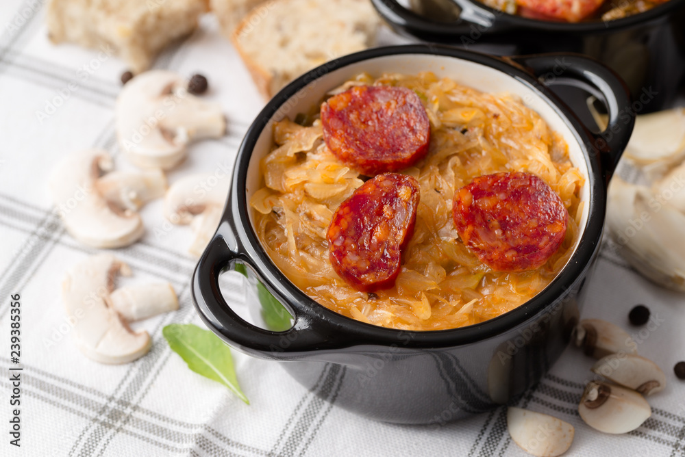 Slovak Christmas national cabbage soup in small black pot with sausage on the tablecloth background.