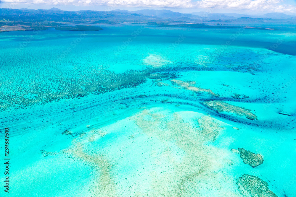 Aerial view of idyllic azure turquoise blue lagoon of West Coast barrier reef, with mountains far in the background, Coral sea, New Caledonia island, Melanesia, South Pacific Ocean.