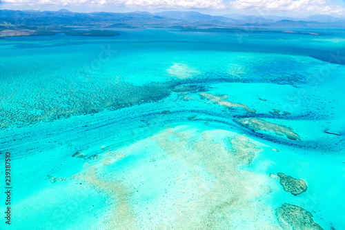 Aerial view of idyllic azure turquoise blue lagoon of West Coast barrier reef, with mountains far in the background, Coral sea, New Caledonia island, Melanesia, South Pacific Ocean.