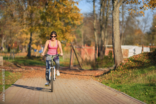 Young beautiful girl in sunglasses and sportswear stands next to a bicycle on the street in the park in autumn.