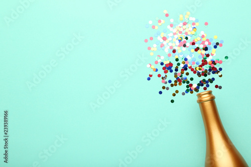 Champagne bottle with colorful confetti on mint background