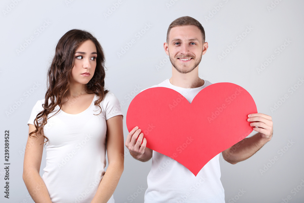 Beautiful young couple holding red paper heart on grey background Beautiful young couple holding red paper heart on grey background