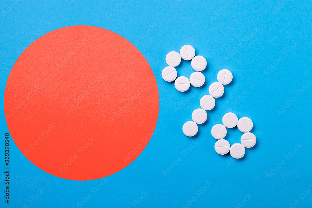 Φωτογραφία A percent sign of pills on a blue background top view with copy space for text, circle of coral color with space for the amount or digits of product discounts
