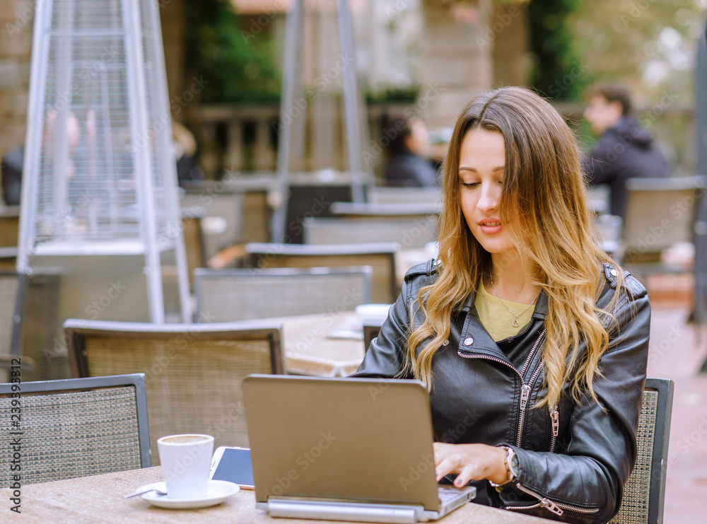 Young lady in stylish outfit smiling while sitting at table in outdoor cafe and browsing modern laptop Young lady in stylish outfit smiling while sitting at table in outdoor cafe and browsing modern laptop