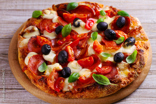 Delicious pizza served on wooden plate. Pizza with pepperoni, tomatoes, cheese, olives and basil